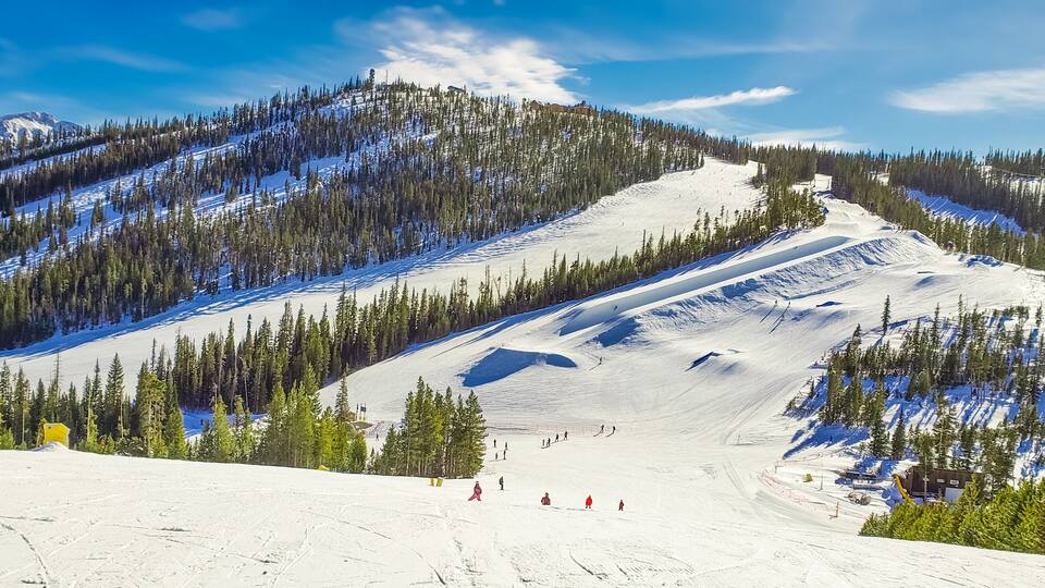 View of ski slope with terrain park and woods in Colorado ski resort on nice winter day; blue sky in background