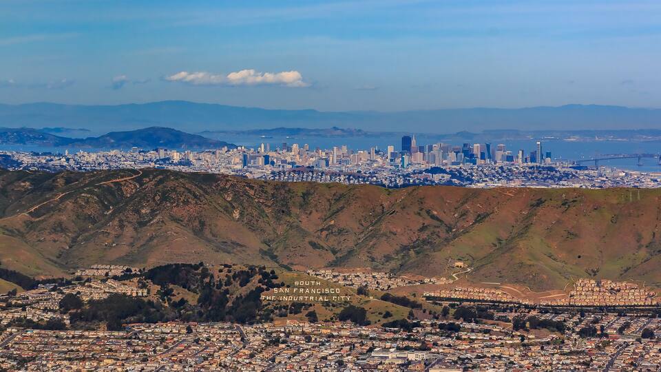 Aerial view of downtown San Francisco and Financial District sky scrapers flying over South San Francisco The Industrial City inscription on San Bruno mountain circa 2015