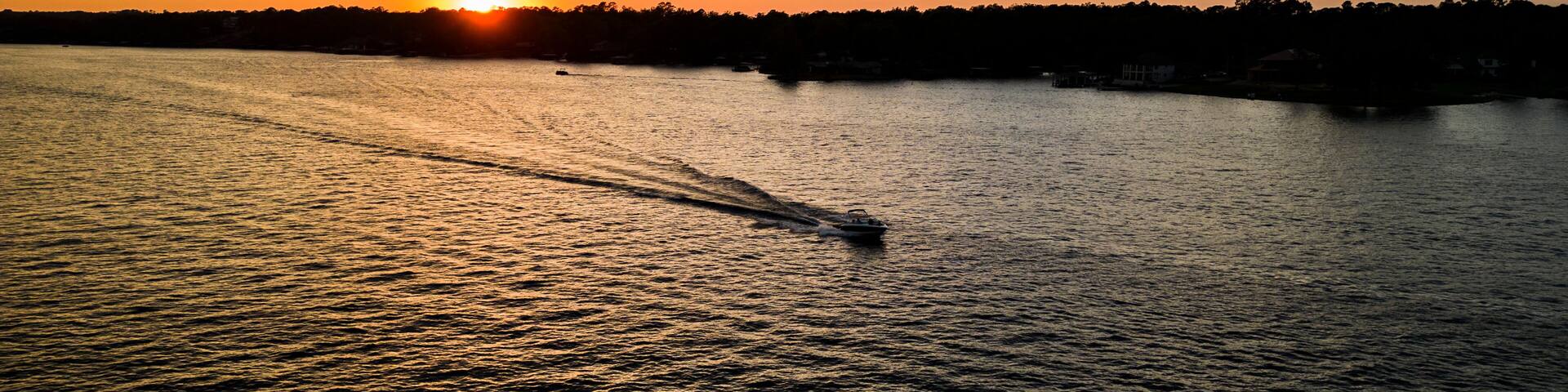 A sunset over a body of water with a boat creating a wake.