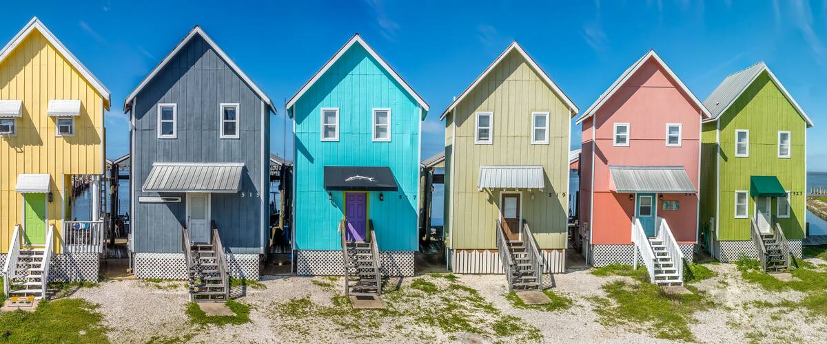 Colorful two story vacation homes with vivid yellow, blue, green, pink paint, wooden steps to door, boat parking structure in back on Dauphin island Alabama