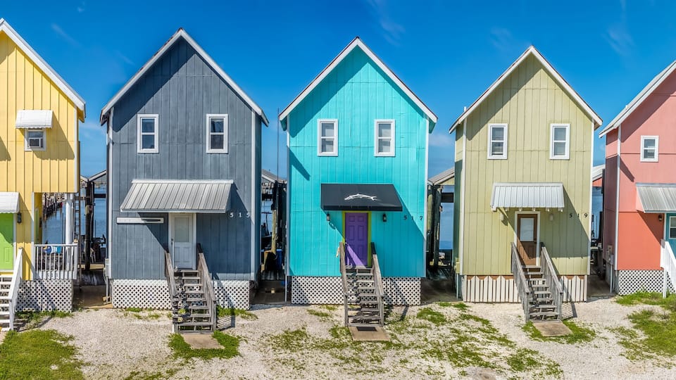 Colorful two story vacation homes with vivid yellow, blue, green, pink paint, wooden steps to door, boat parking structure in back on Dauphin island Alabama