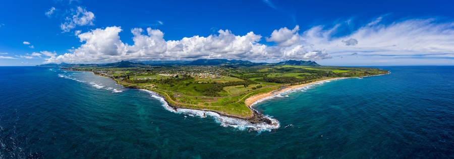 Vista aérea de una isla costera con cielo azul despejado, una playa de arena y exuberantes paisajes verdes.