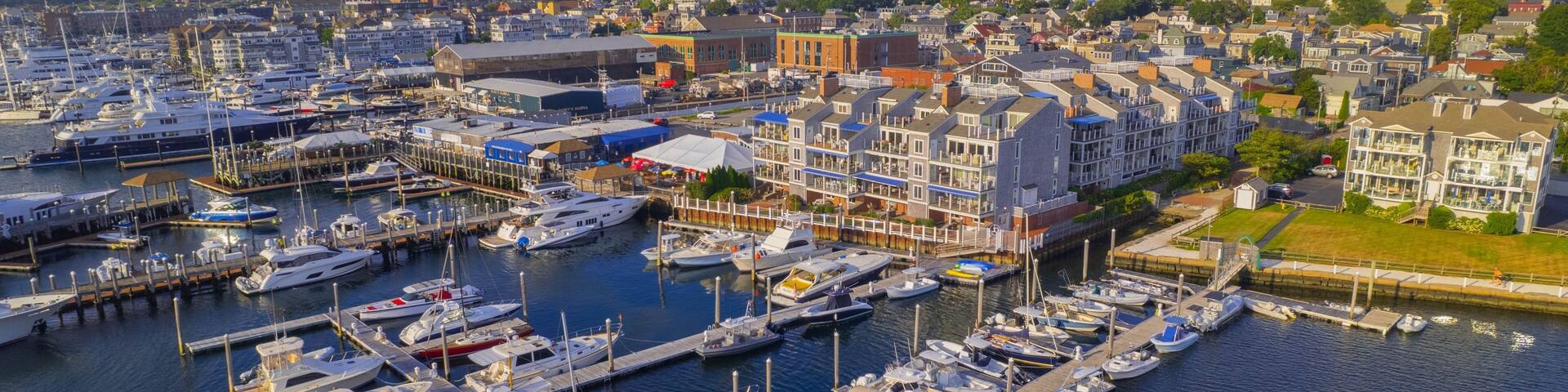 A marina with numerous boats docked, surrounded by residential buildings and a church spire in the distance.