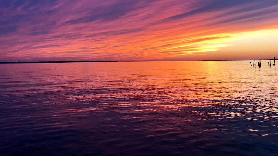 A sunset over a calm body of water with a pier extending into the water.