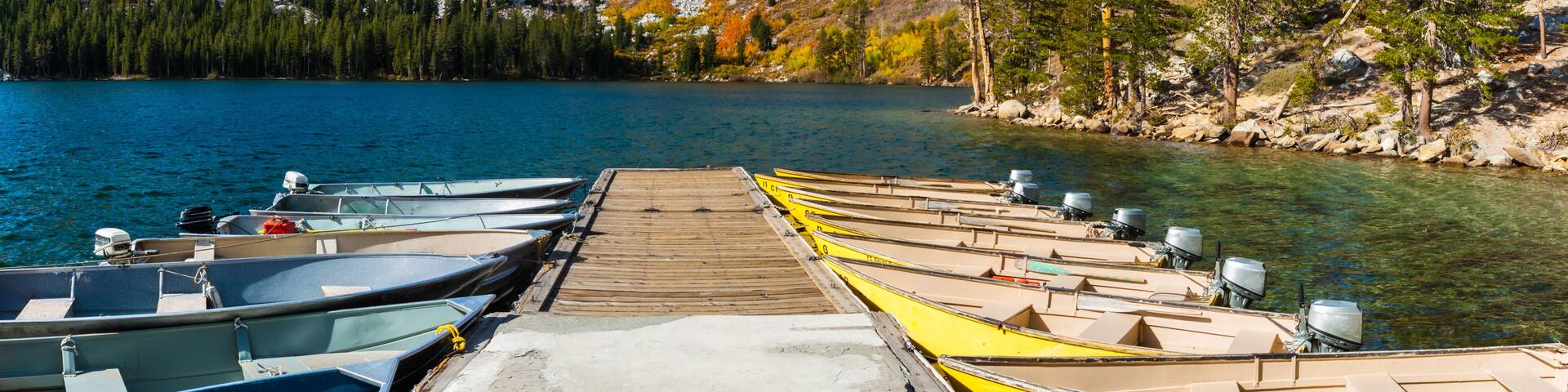 A row of canoes docked at a pier with a mountainous backdrop.