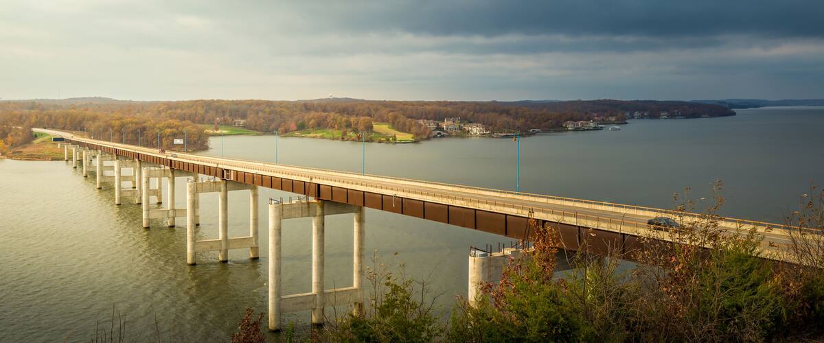 A long bridge over a calm river with a forested landscape in the background.