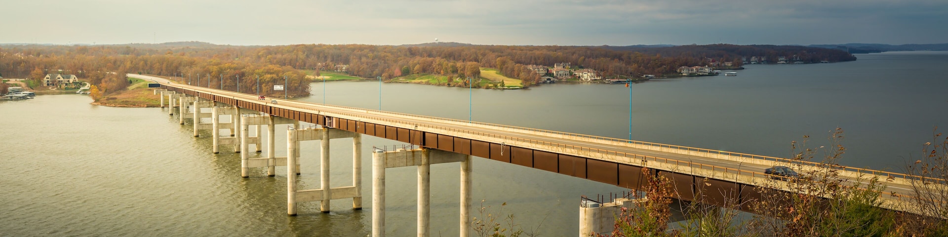 A long bridge over a calm river with a forested landscape in the background.