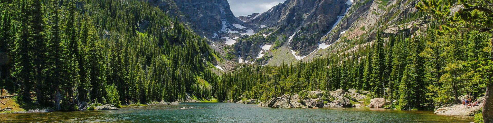 A clear mountain lake surrounded by dense forest and rocky mountains.