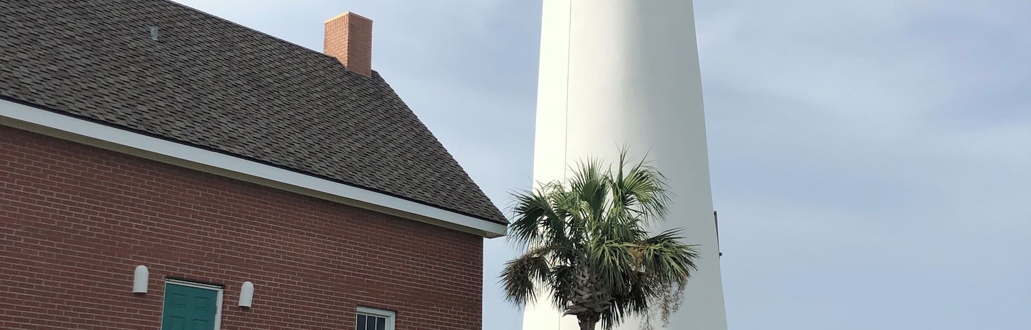 Um edifício de tijolos com uma escadaria e um farol branco ao fundo.