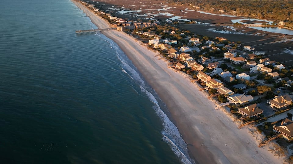An aerial view of a coastal town with a beach, houses, and a pier.