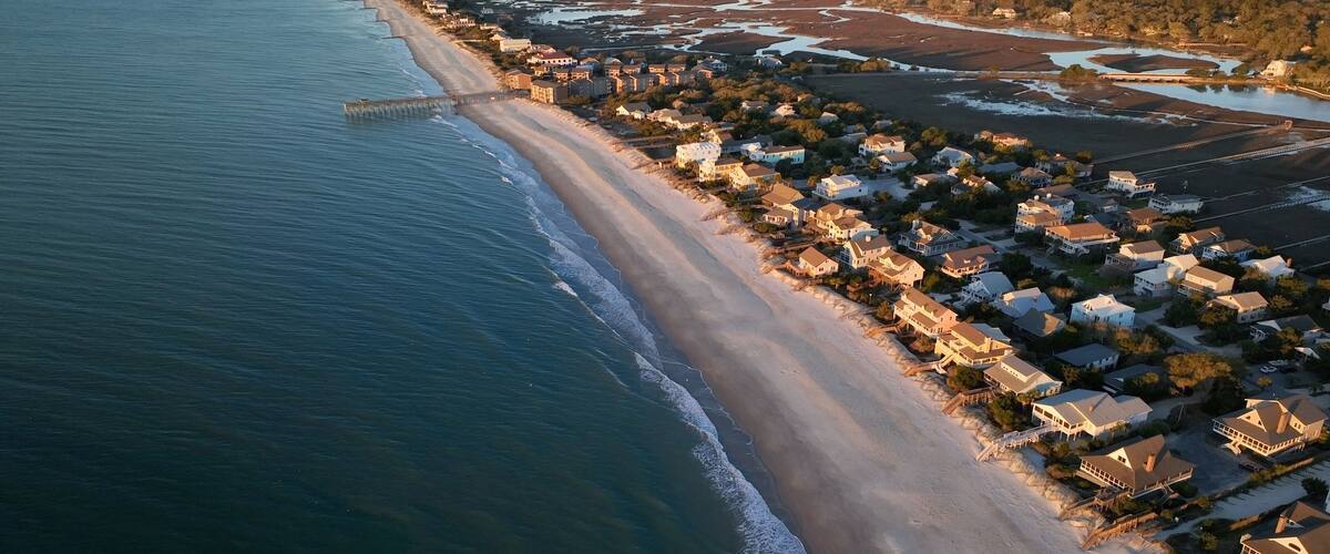 An aerial view of a coastal town with a beach, houses, and a pier.