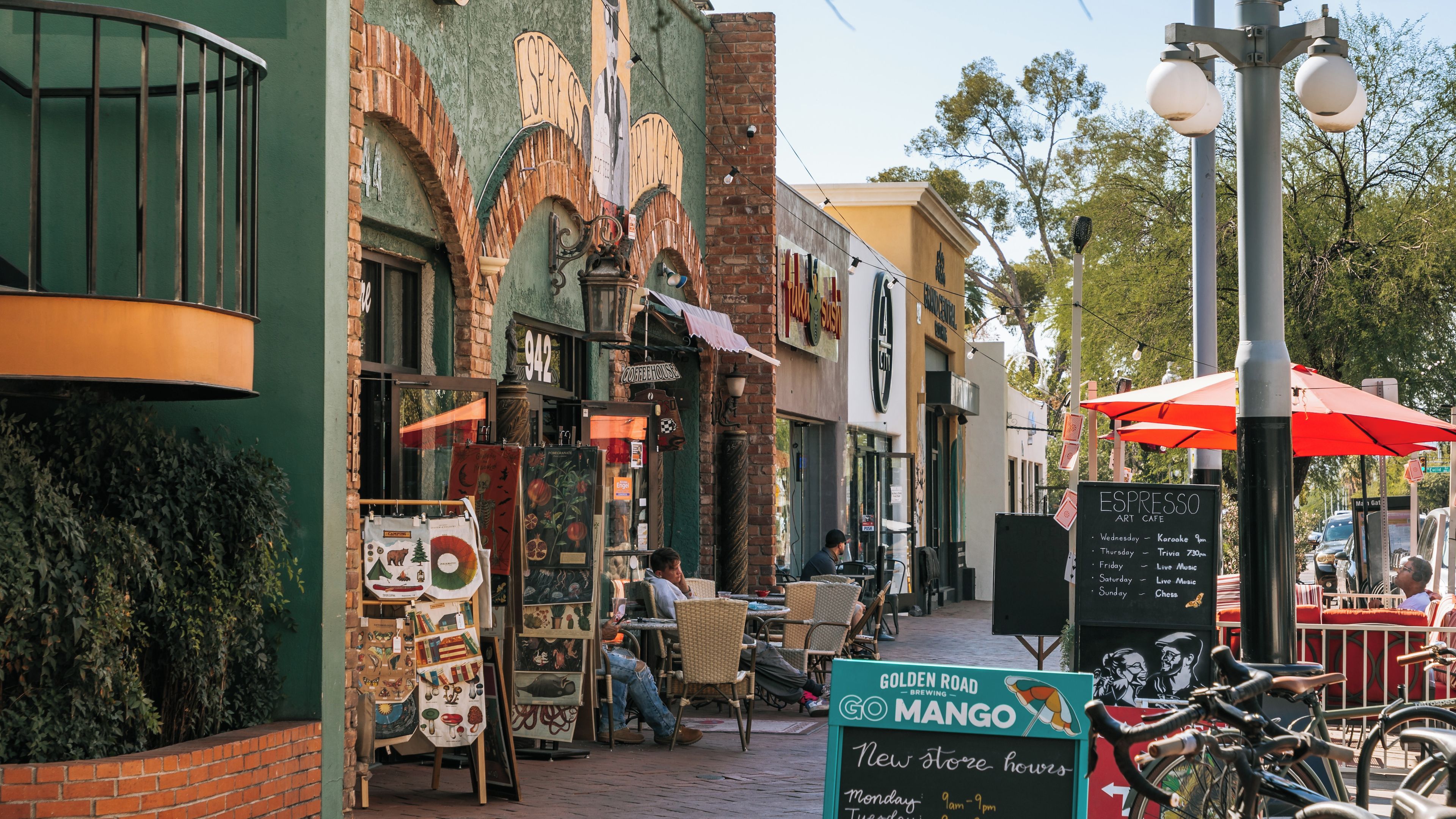 Una calle con mesas al aire libre, una cafetería y un cartel de Golden Road Brewing Mango.