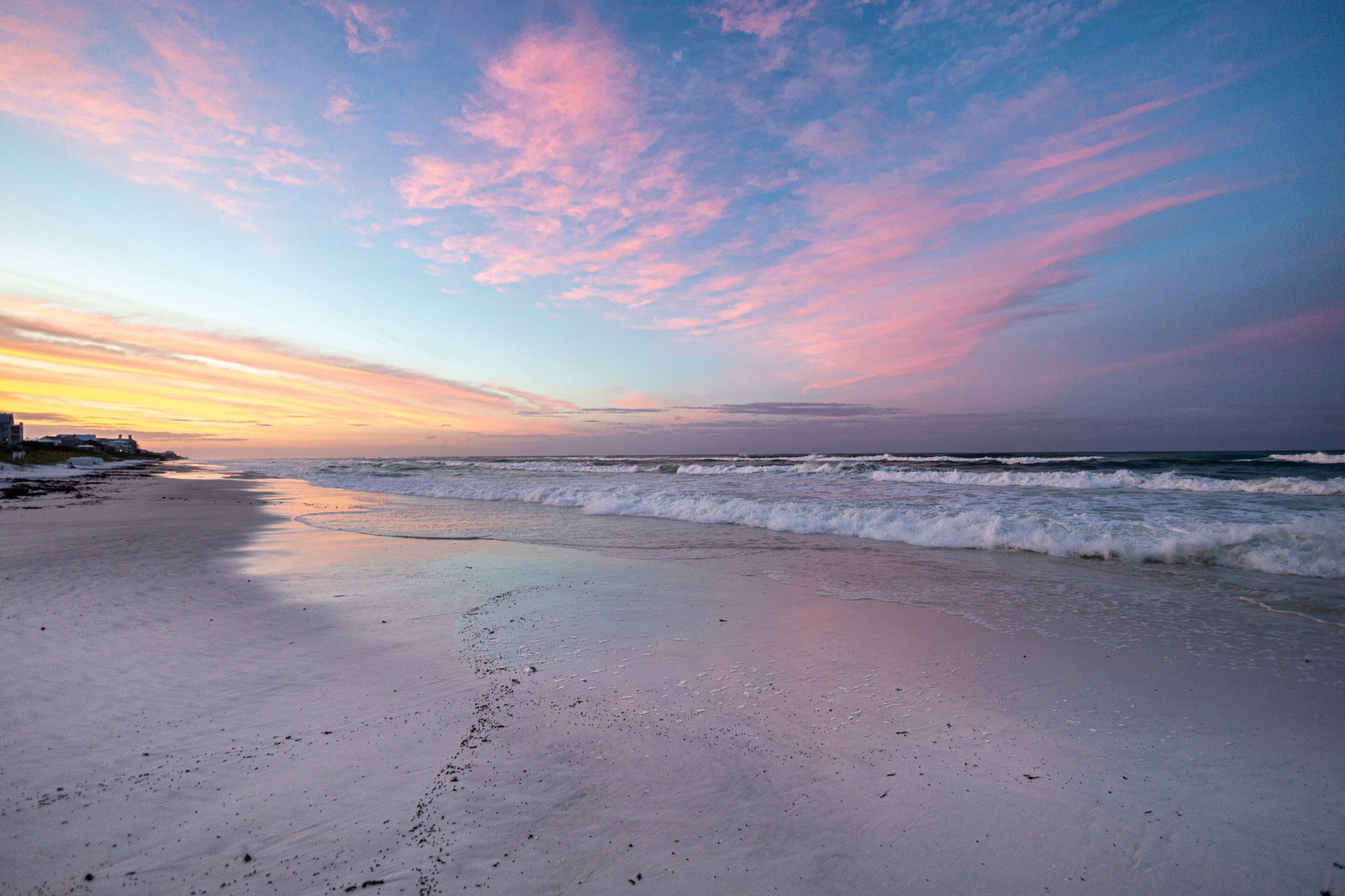 A beach with waves at sunset, a clear sky, and distant land.