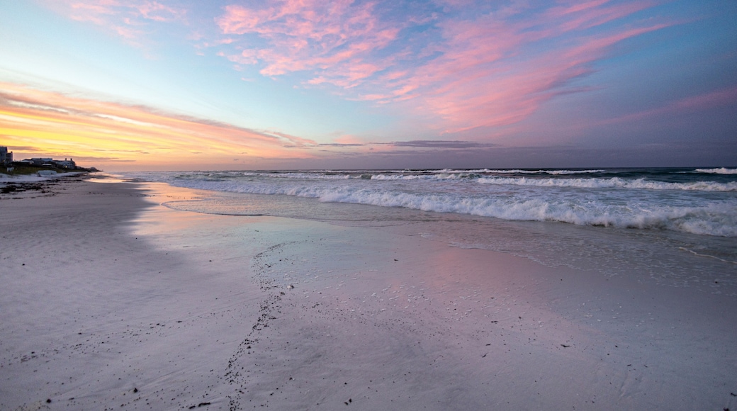 A beach with waves at sunset, a clear sky, and distant land.