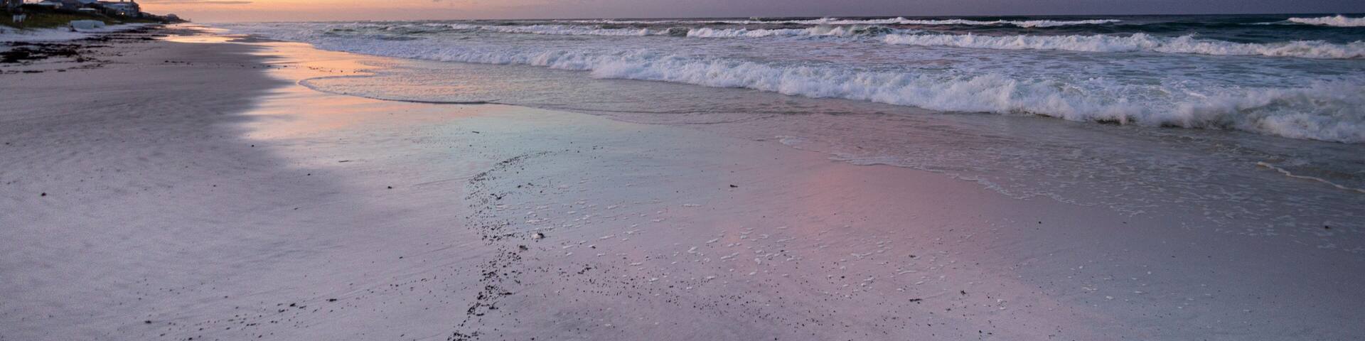 A beach with waves at sunset, a clear sky, and distant land.