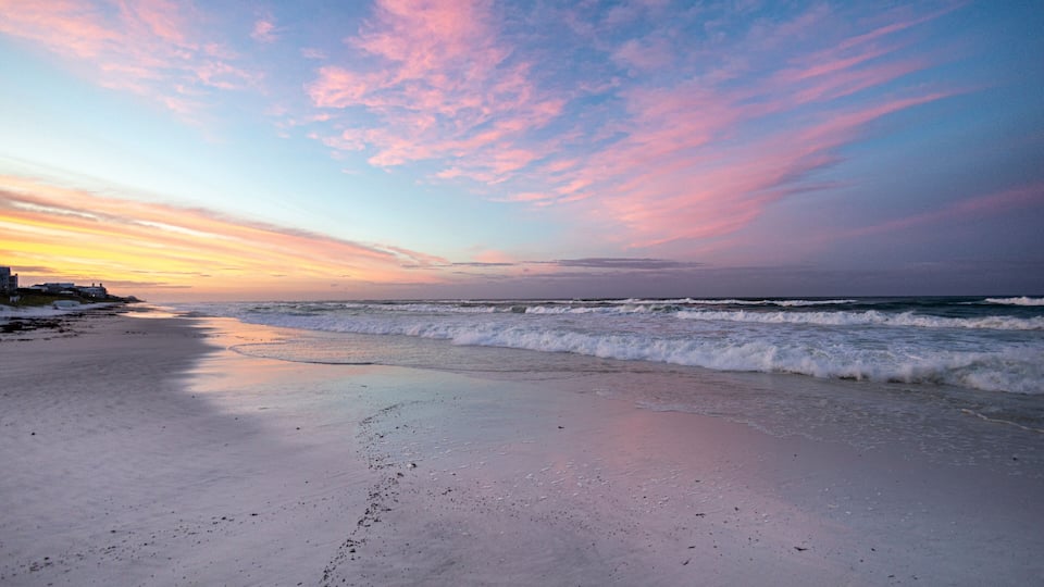A beach with waves at sunset, a clear sky, and distant land.