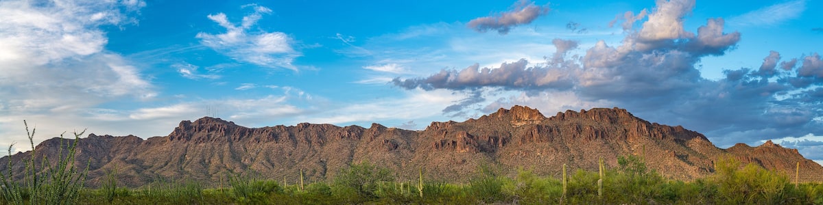 A mountain range with sparse vegetation and a clear blue sky with scattered clouds.
