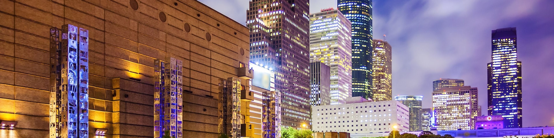 Silhueta urbana com edifícios iluminados, um rio e uma ponte.
