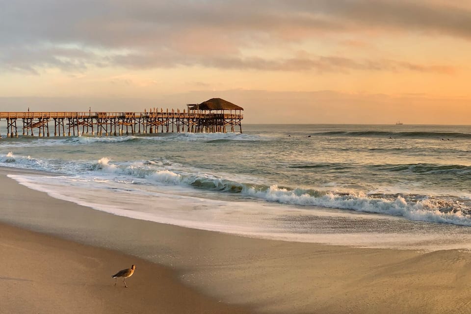 A beach with waves, a pier, and a sunset.