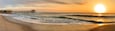 A beach with waves, a pier, and a sunset.