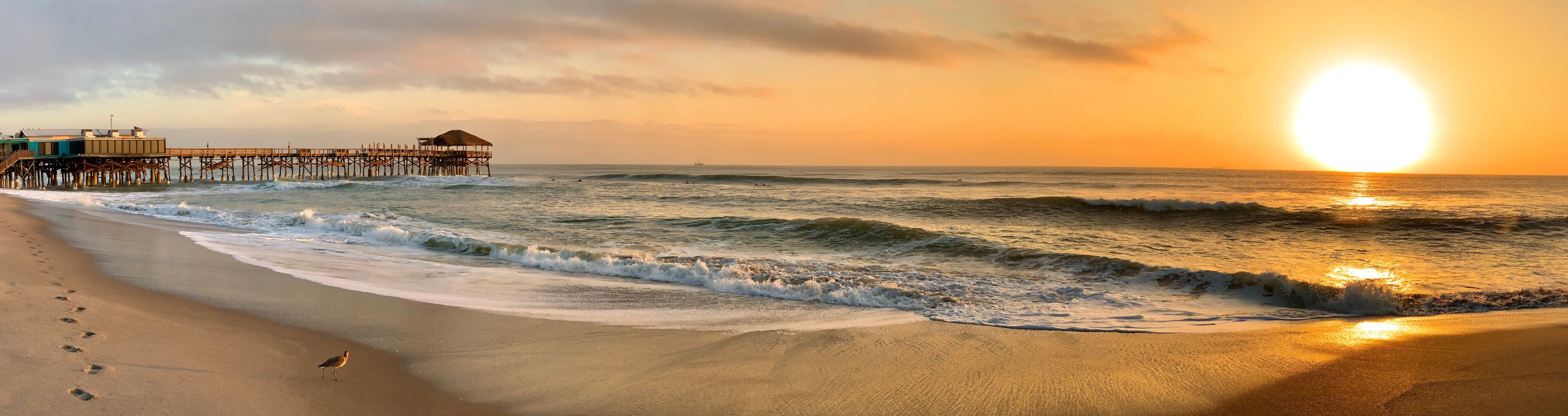 A beach with waves, a pier, and a sunset.