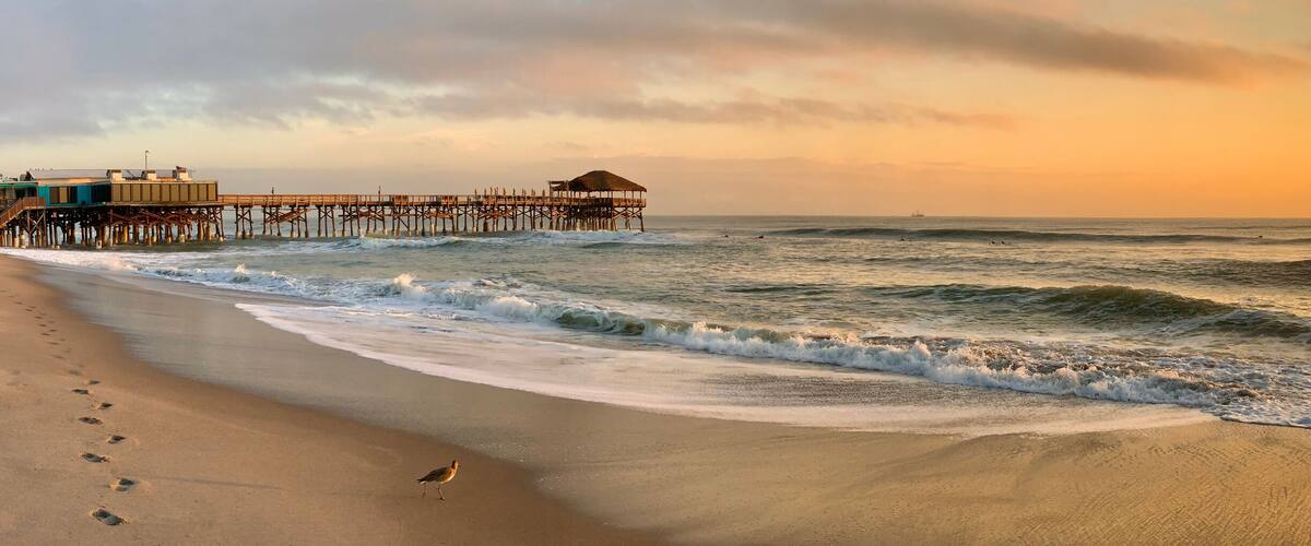A beach with waves, a pier, and a sunset.