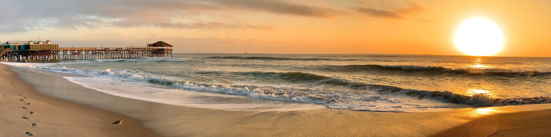 A beach with waves, a pier, and a sunset.