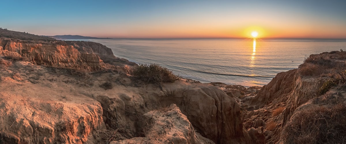 A coastal landscape with cliffs and a sunset over the ocean.
