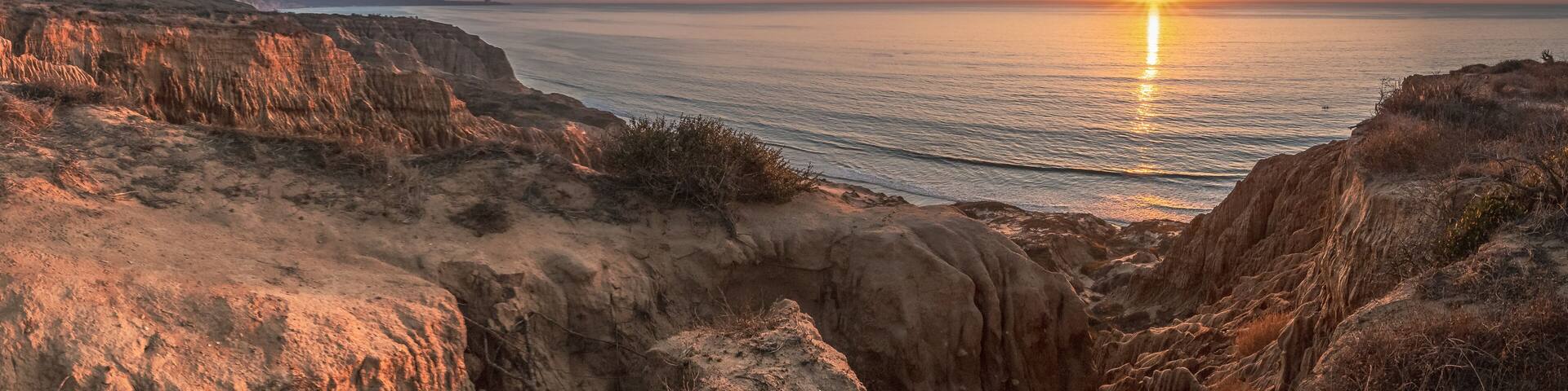 A coastal landscape with cliffs and a sunset over the ocean.