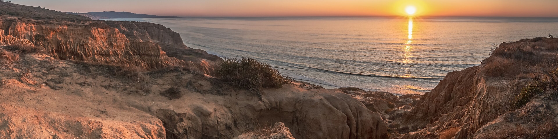 A coastal landscape with cliffs and a sunset over the ocean.