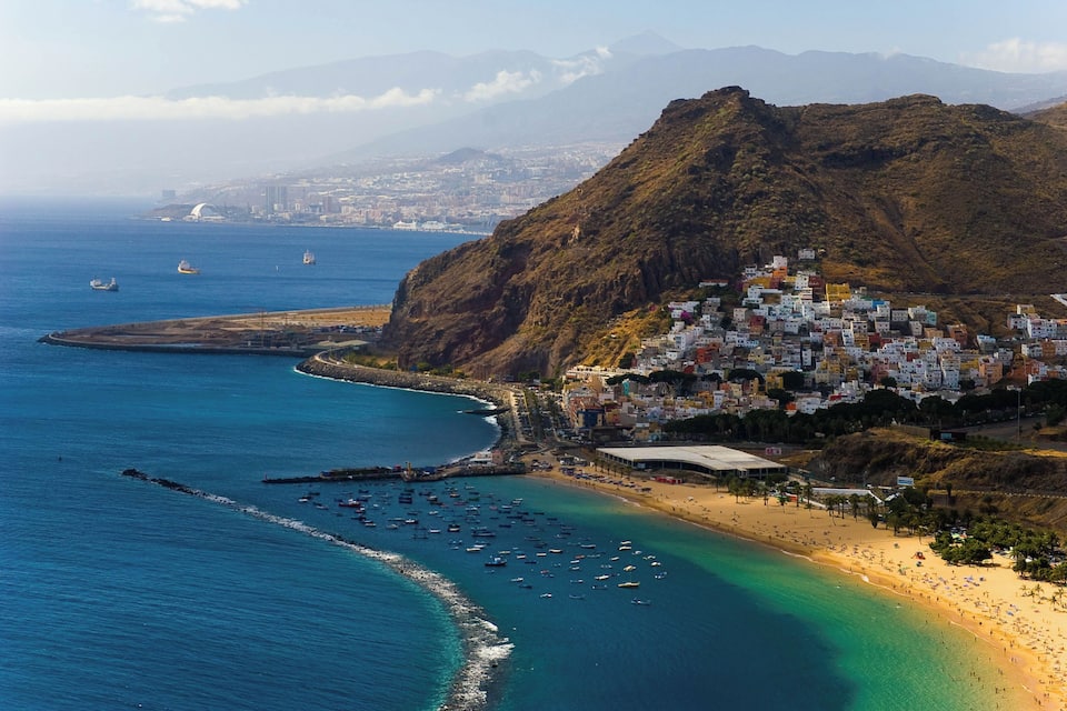 Un pueblo costero con playa, barcos y montañas al fondo.