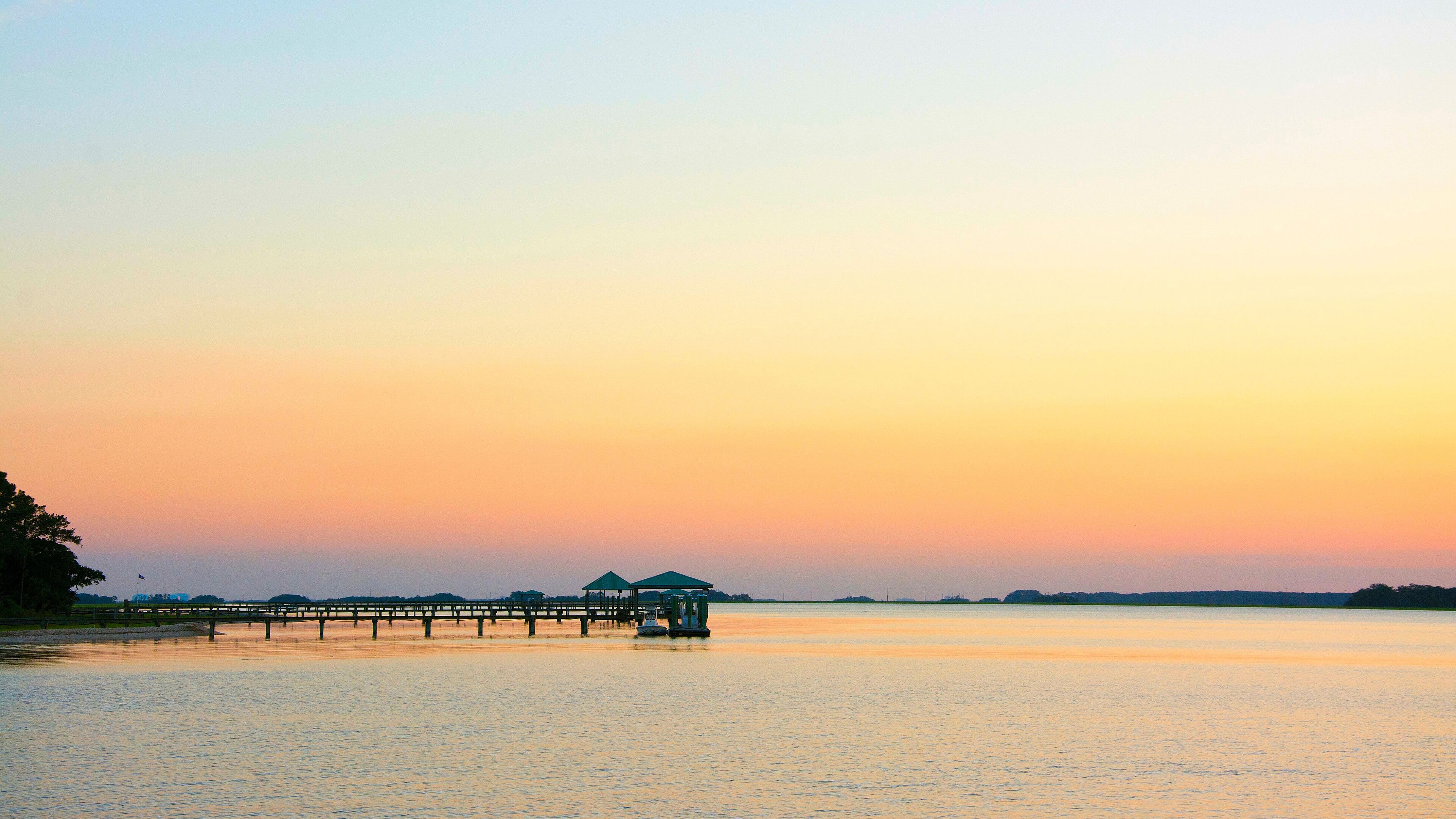 A sunset over a calm lake with a wooden pier extending into the water.