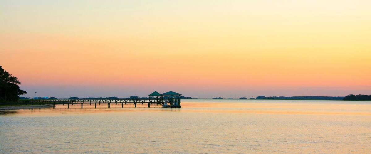 A sunset over a calm lake with a wooden pier extending into the water.