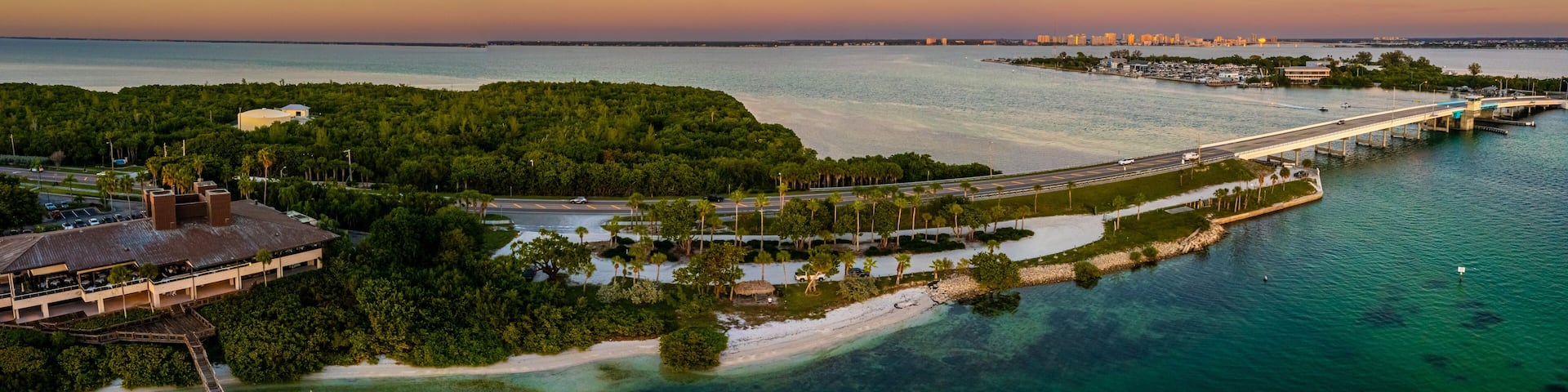 A coastal cityscape with a bridge, marina, and lush greenery.