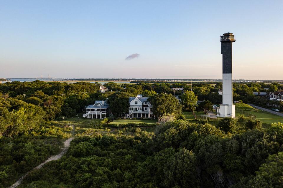 A lighthouse, two large white houses, and a dense forest.