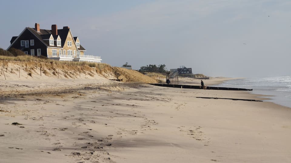 A beach with a large house and dunes.