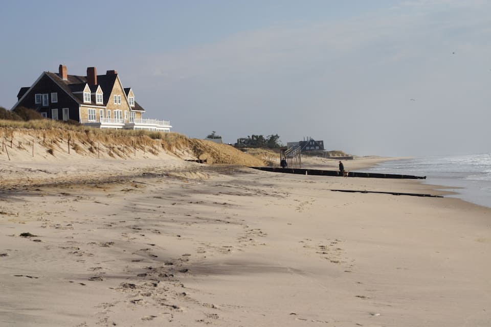 A beach with a large house and dunes.