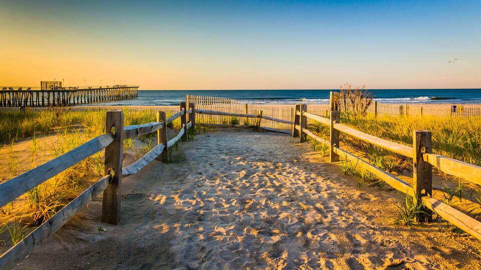 A sandy beach with wooden fences and a pier in the background.