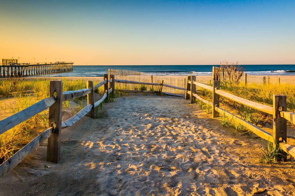 A sandy beach with wooden fences and a pier in the background.