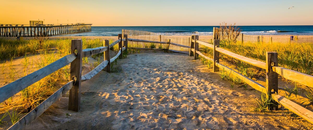 A sandy beach with wooden fences and a pier in the background.