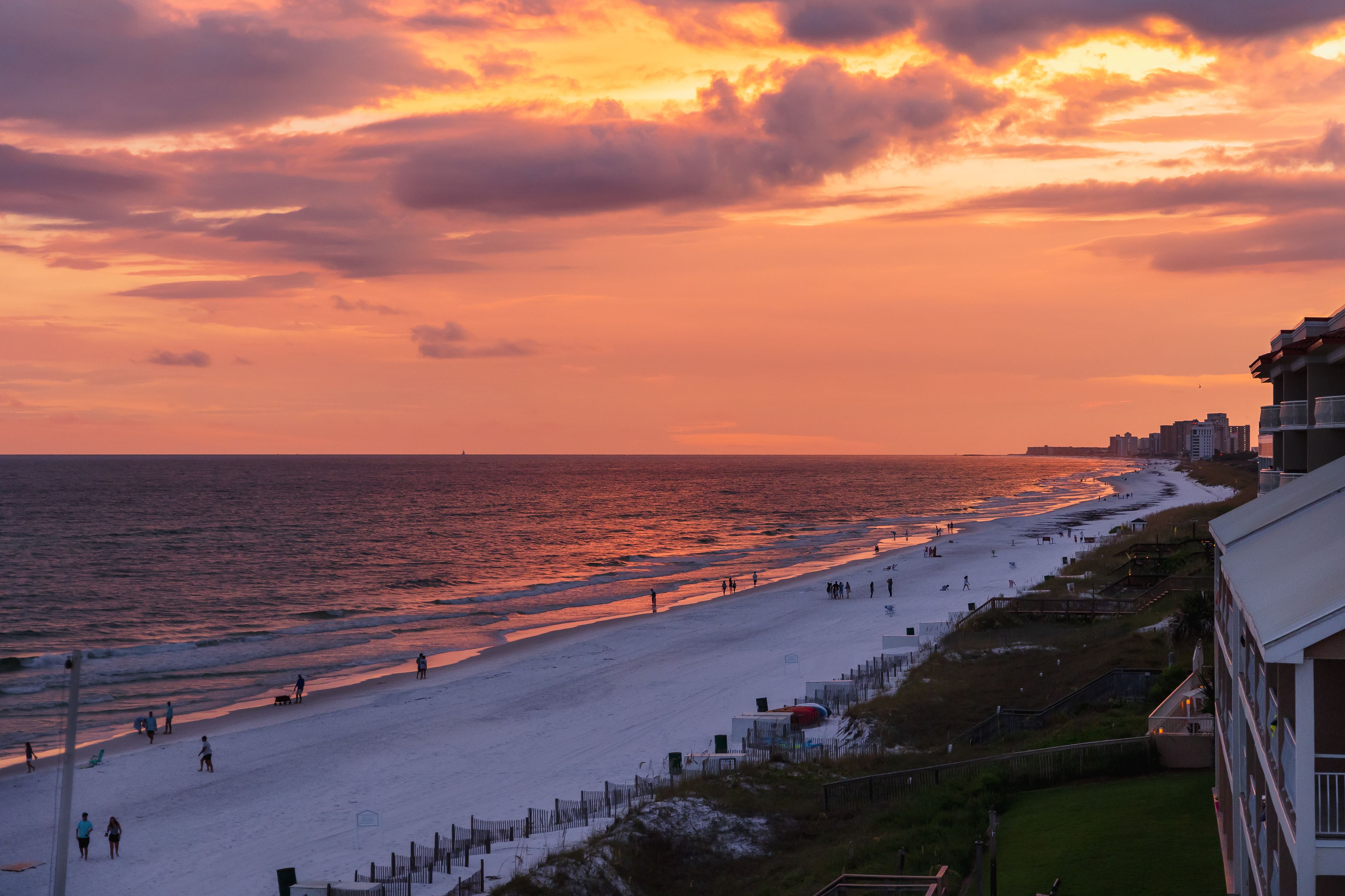 A beach with people walking and a sunset in the background.