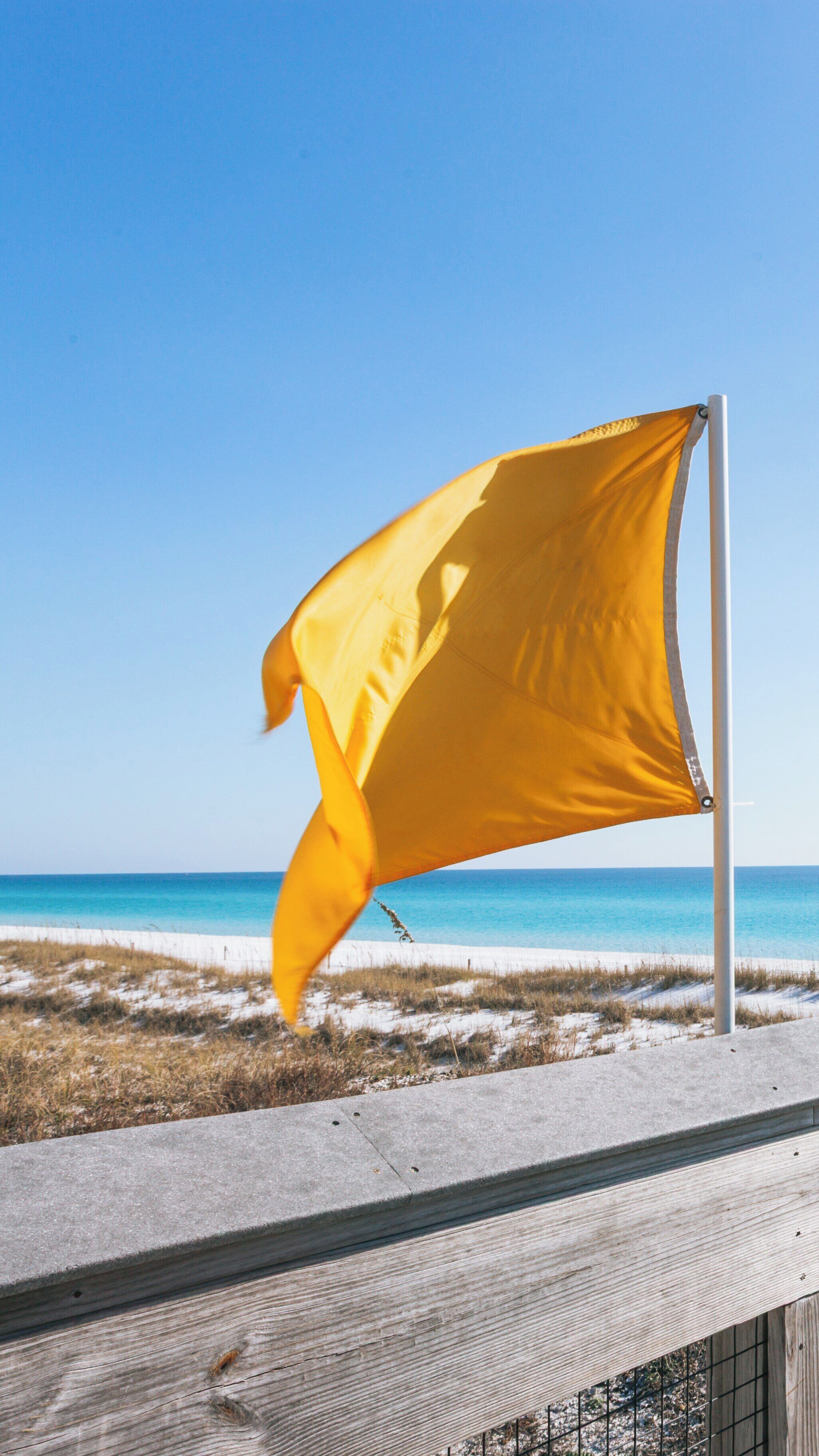 Vibrant yellow flag waving at Henderson Beach State Park during a clear day in Fort Walton Beach, Florida with turquoise water in the background