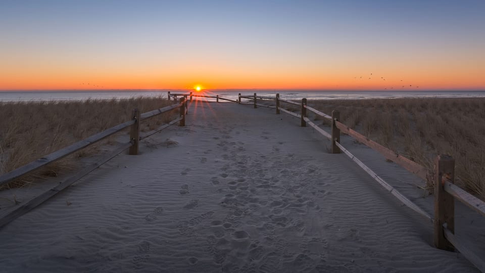 A beach path leading to the ocean at sunset with footprints in the sand.