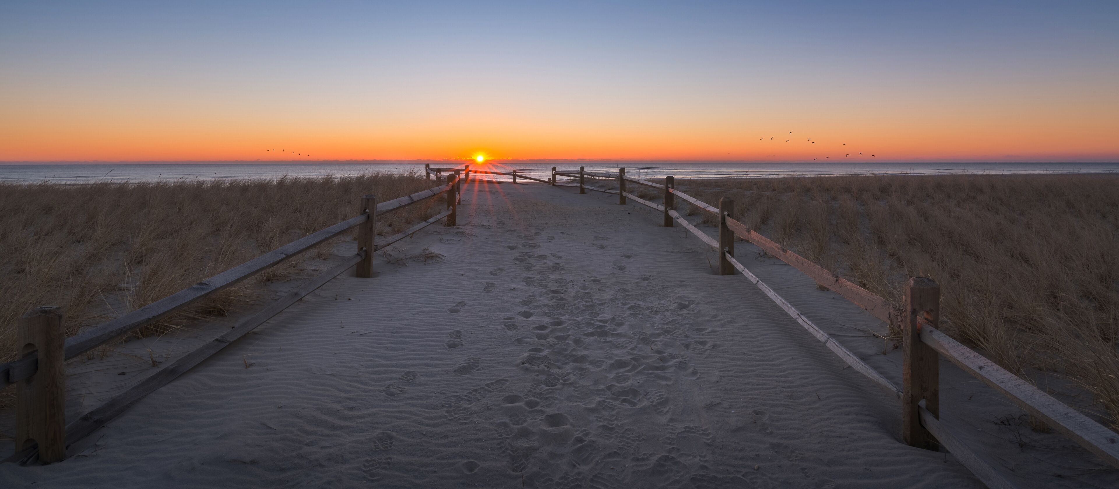 A beach path leading to the ocean at sunset with footprints in the sand.
