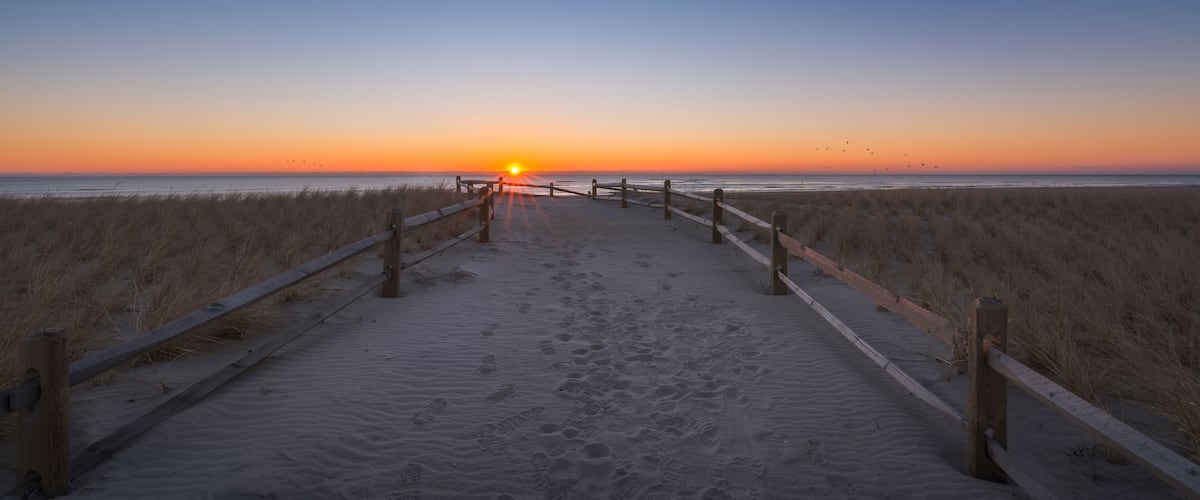 A beach path leading to the ocean at sunset with footprints in the sand.