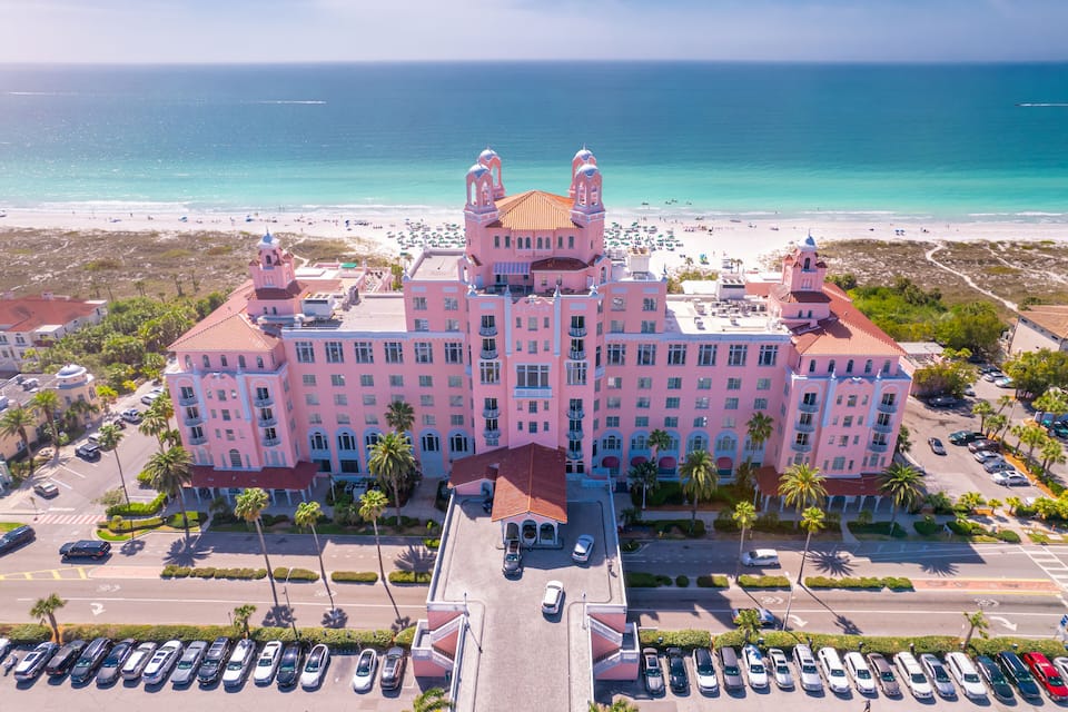 A pink hotel with a beach and ocean in the background.