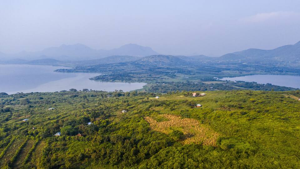 A lush green landscape with scattered houses and a large body of water surrounded by hills.