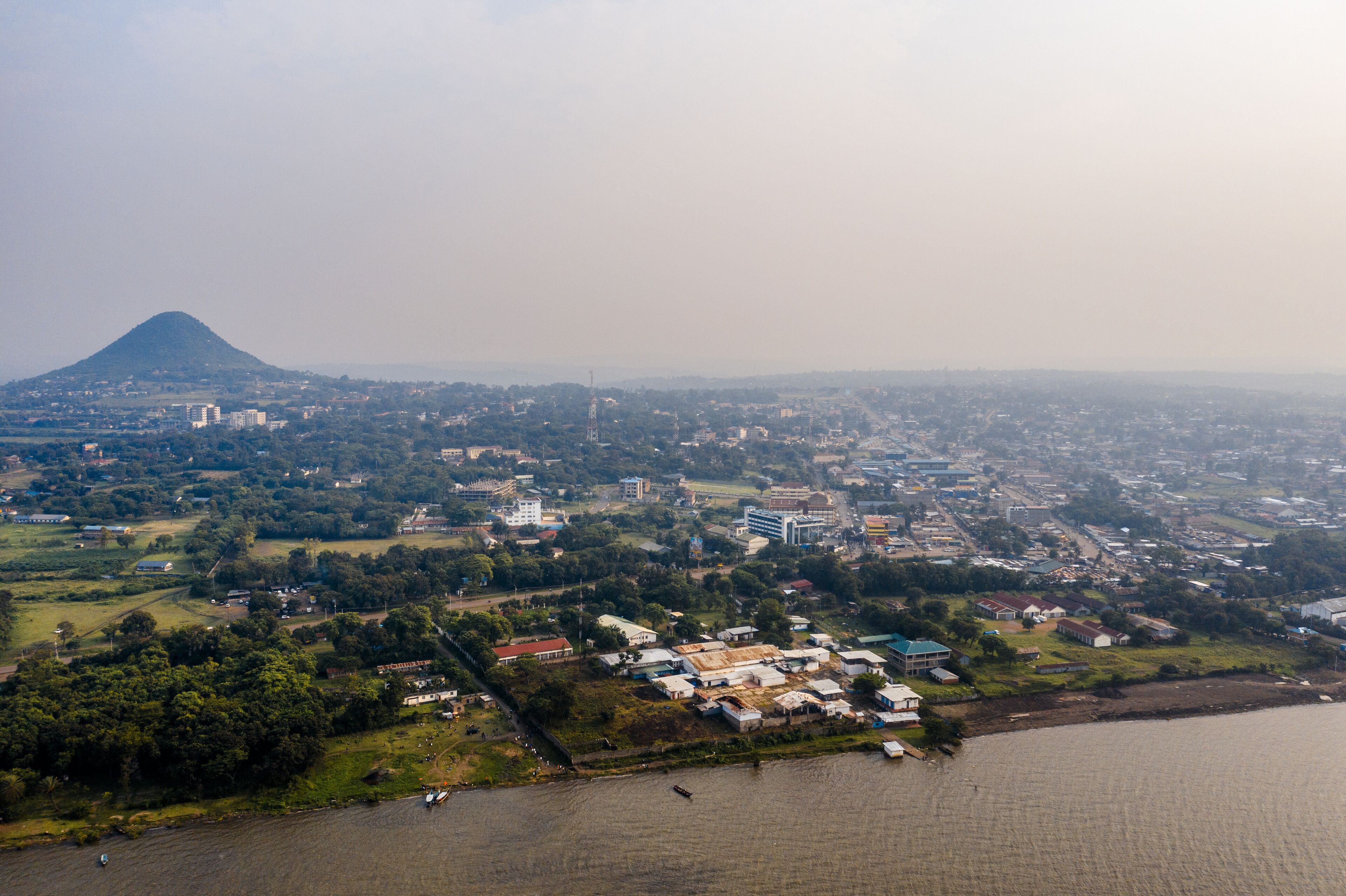 An aerial view of a coastal city with a prominent hill in the background, a river, and scattered buildings.