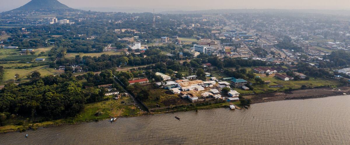 An aerial view of a coastal city with a prominent hill in the background, a river, and scattered buildings.