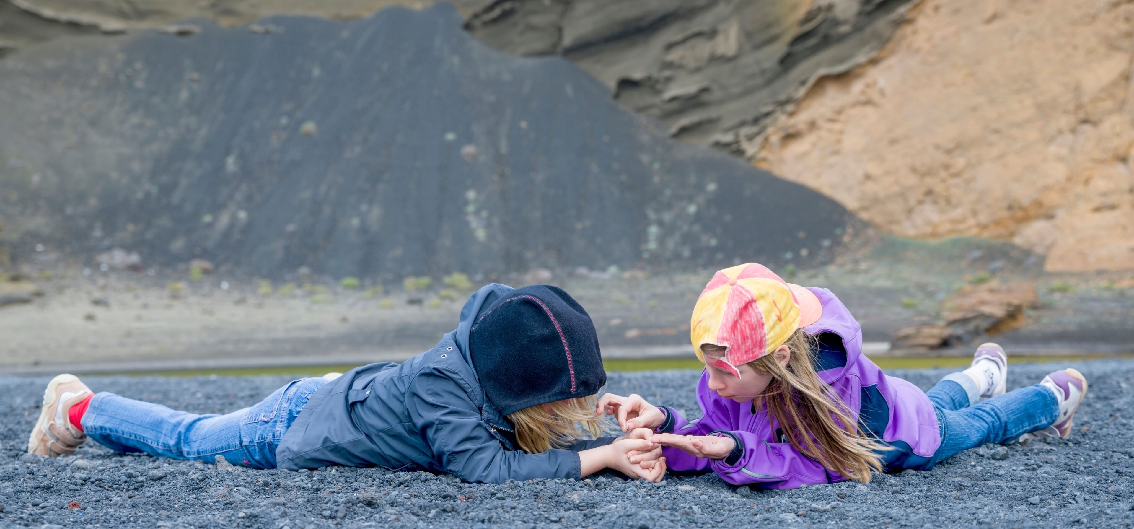 Two people lying on a beach with rocky cliffs in the background.